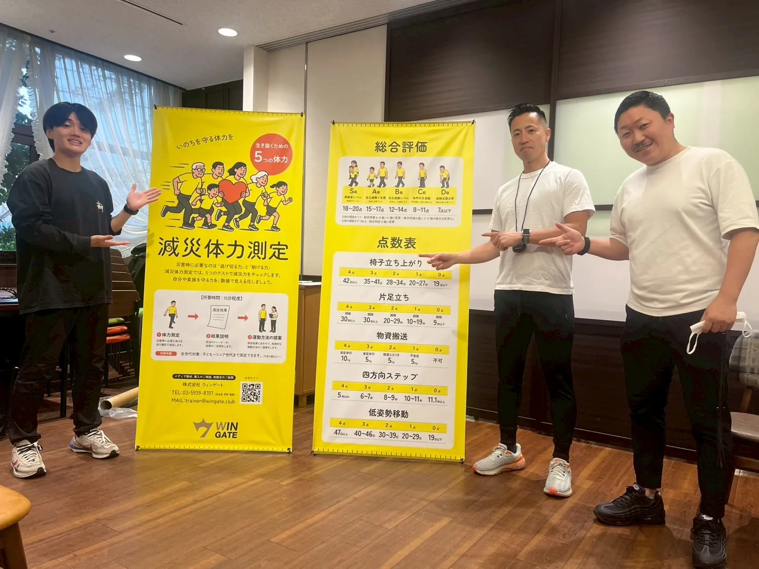 減災体力測定の案内バナーと評価点数表の前に立つWIN GATEスタッフ