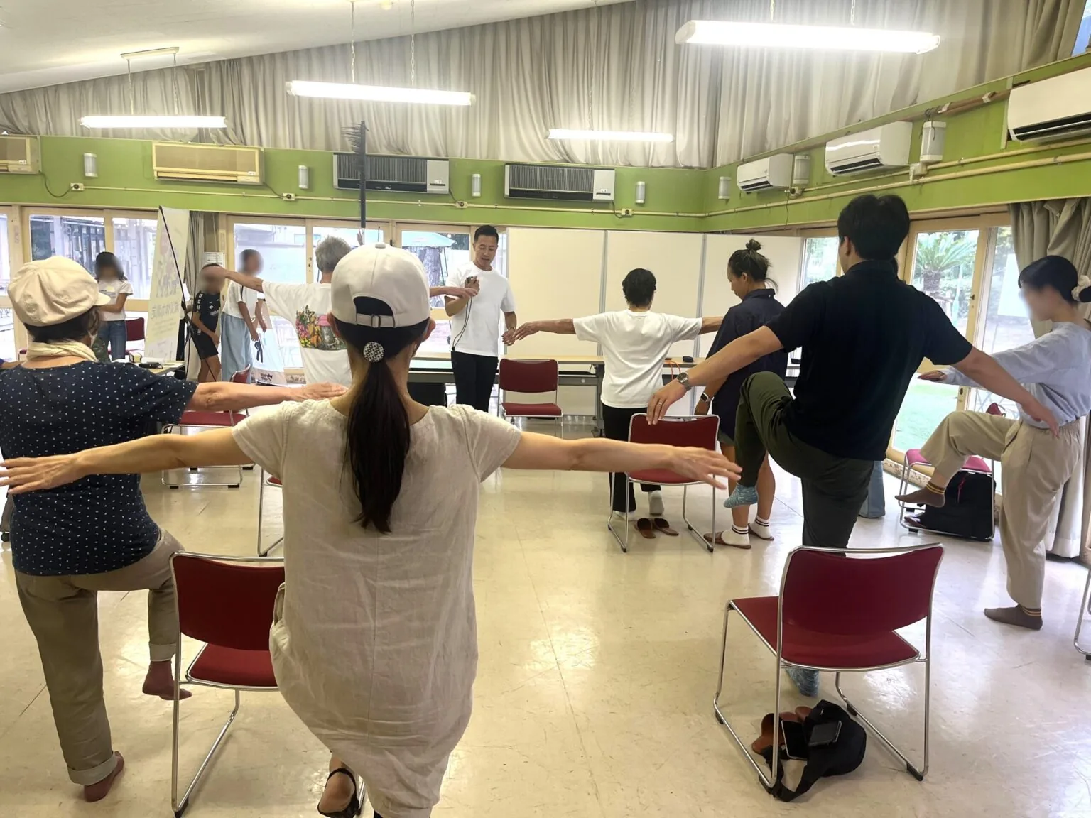 インストラクターの指導のもと、参加者が腕を広げてバランス運動に取り組む様子(顔は加工処理済み)